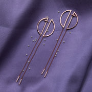 a pair of circle shaped rose gold color silver earrings dangler laid over a purple fabric with pearls sprinkled around it